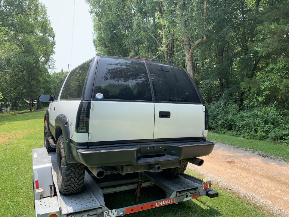 White 1995 Chevrolet Tahoe SUV with tinted windows, on a U-Haul trailer, rear view