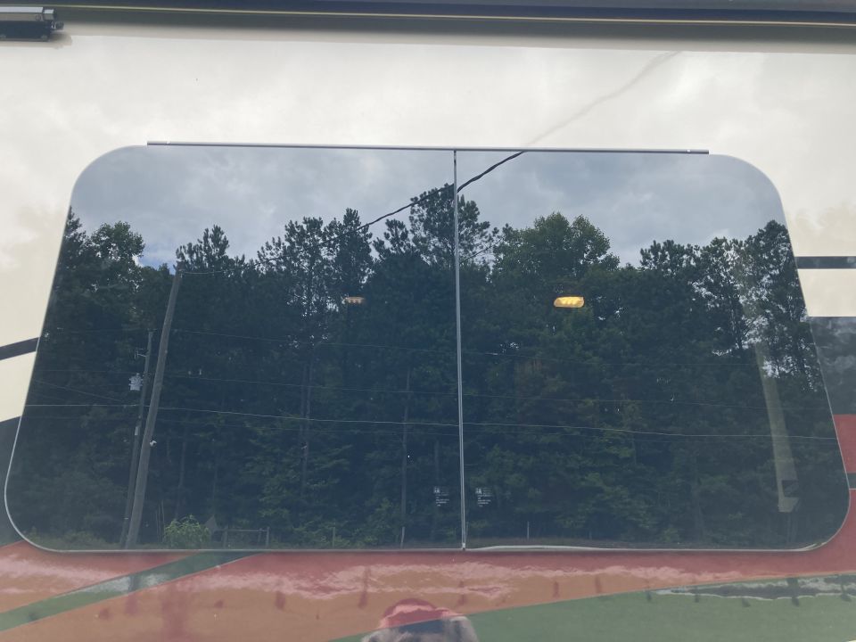 Tinted RV window reflecting trees and sky