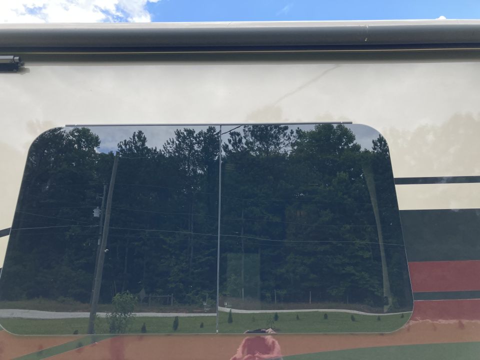 Reflection of trees and sky in a tinted RV window. Supermotors.net logo visible at bottom right