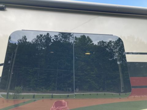 2015 Ford F-550 - Reflection in the tinted window of an RV shows a wooded area and a cloudy sky.