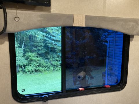 2015 Ford F-550 - Looking out an RV window at a wooded area and a blue-tinted reflection of a building.