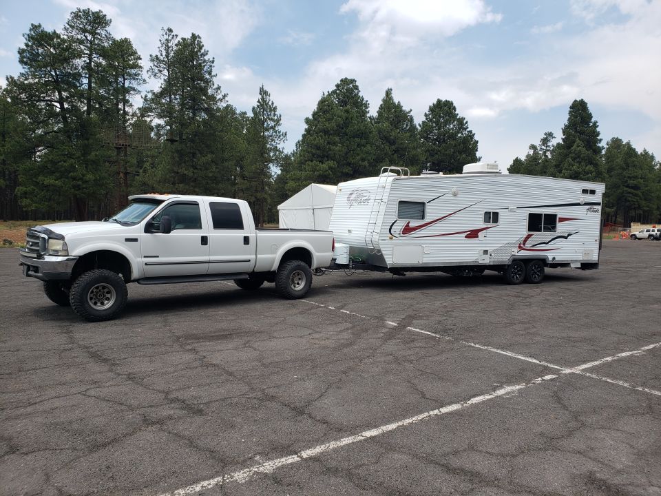 White 2000 Ford F-350 Super Duty crew cab pickup truck with aftermarket wheels, towing a white travel trailer with red graphics