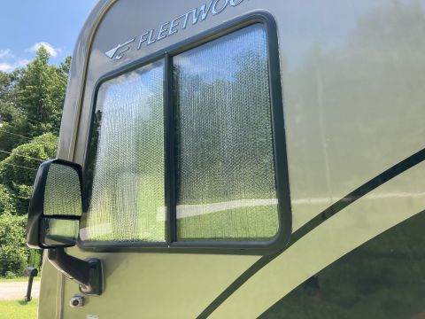 2015 Ford F-550 - Side view of an RV window with a reflective shade and Fleetwood branding.