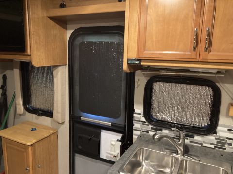 2015 Ford F-550 - Interior view of an RV showing cabinetry, a door, a window with a reflective shade, and a sink area.