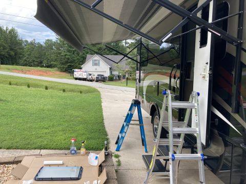2015 Ford F-550 - A removed RV door window sits on cardboard next to cleaning supplies, with ladders and the RV itself in the background.