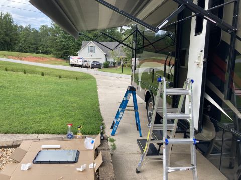 2015 Ford F-550 - RV awning repair in progress with ladders and a removed window part on the ground.