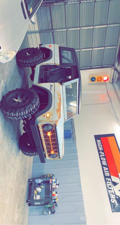 1976 Ford Bronco - A white 1976 Ford Bronco with visible rust and off-road tires sits in a garage.