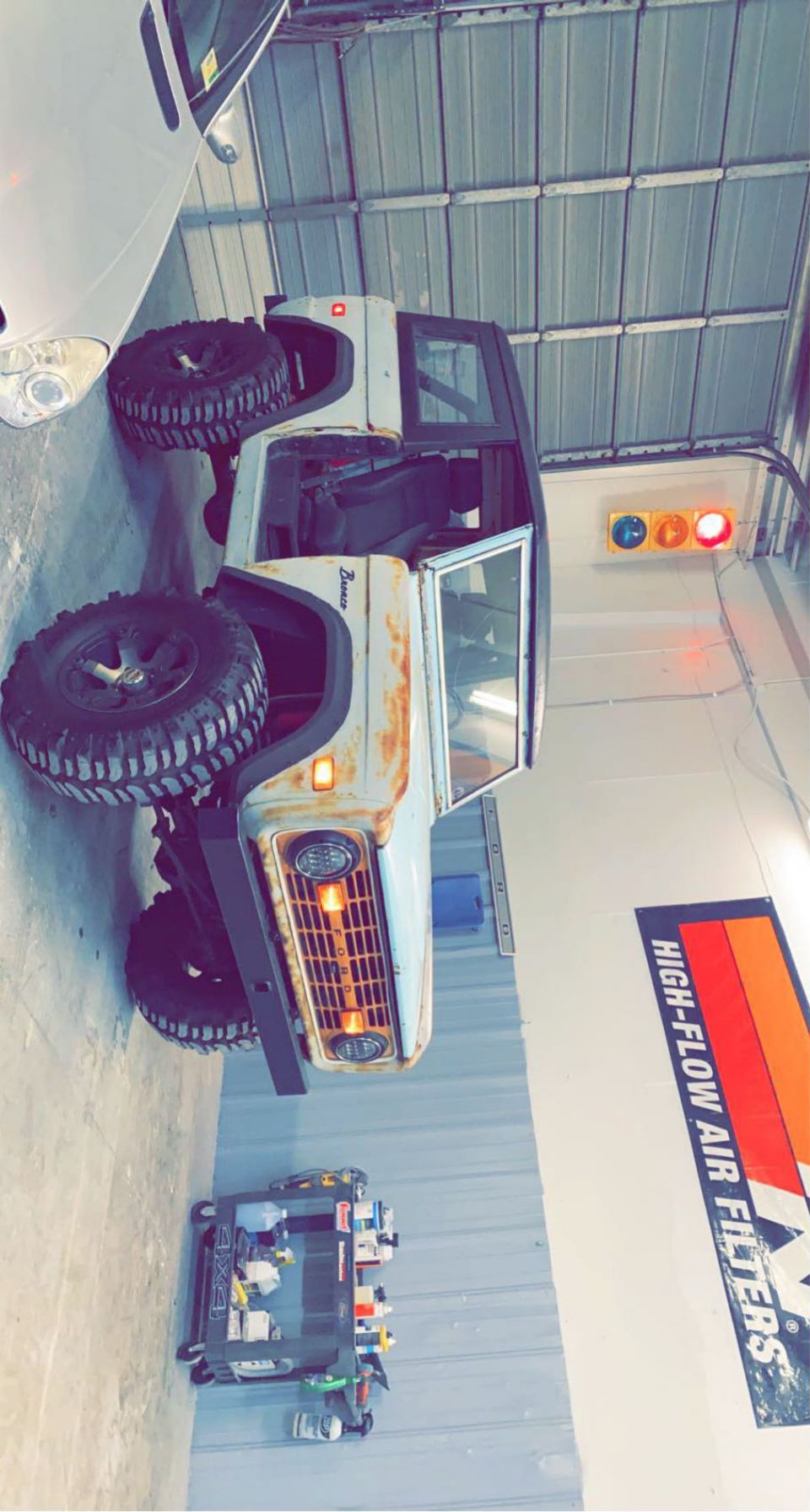 White 1976 Ford Bronco with rust spots, lifted suspension, and large off-road tires parked indoors
