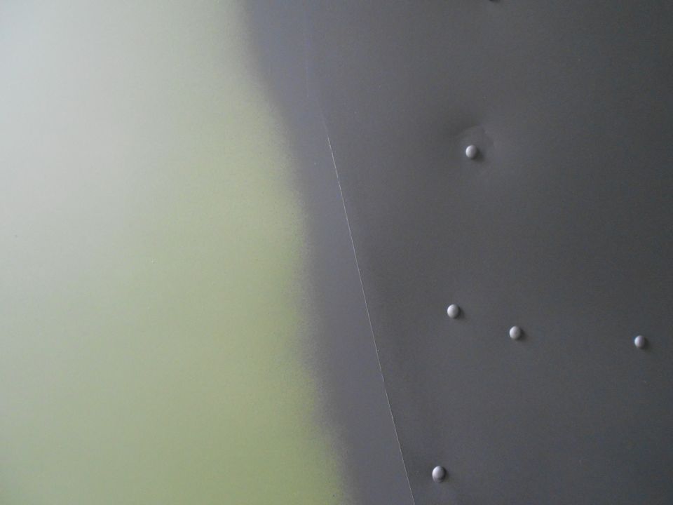 Close-up of a gray metal panel with rivets and a faint greenish area on the left