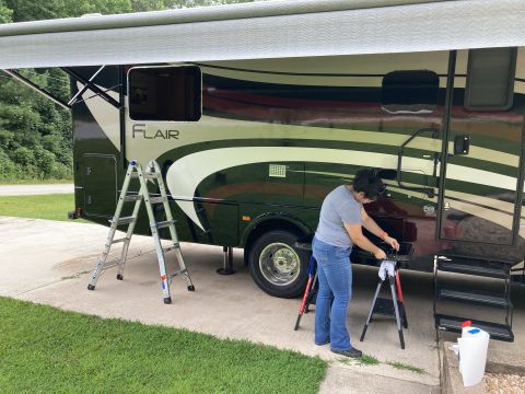 2015 Ford F-550 - A person works on the exterior of a Flair motorhome, with ladders and supplies nearby.