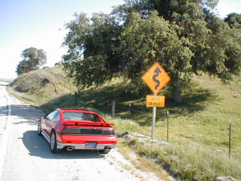 1986 Pontiac Fiero - 1986 Pontiac Fiero parked on a rural road next to a curve warning sign.