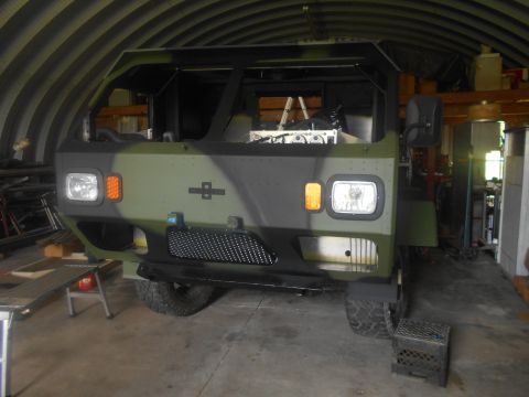 1992 Ford Bronco - Camouflaged military truck parked indoors with the hood open, revealing engine parts.