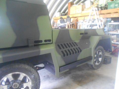 1992 Ford Bronco - This custom vehicle, painted in camouflage, is parked indoors with shelves and equipment in the background.