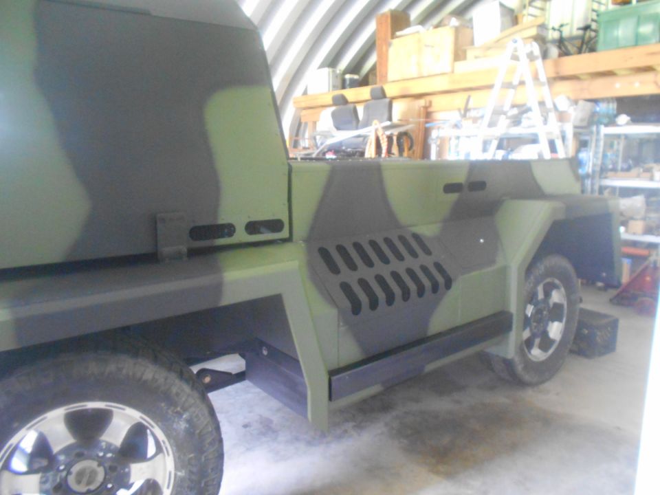 Custom camouflage vehicle in a garage, side view. Looks like a modified truck or SUV
