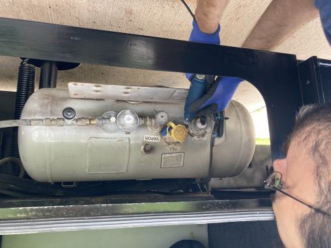 2015 Ford F-550 - Close-up of a propane tank's fittings, with hands wearing blue gloves adjusting a valve.