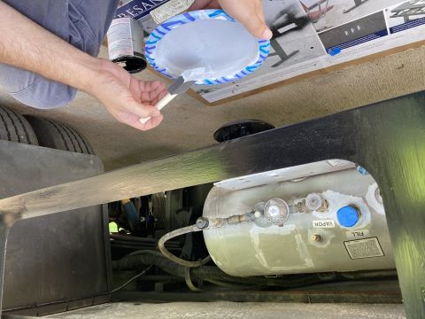 2015 Ford F-550 - A person is painting a black metal beam above a large propane tank mounted to the underside of a vehicle. The tank has visible fill and vap…