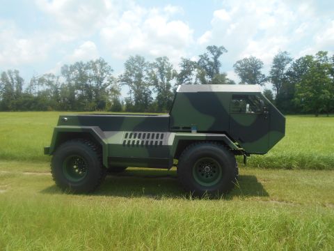 1992 Ford Bronco - A camouflaged military truck with a flatbed is parked in a grassy field under a cloudy sky.