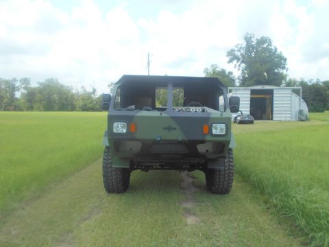 1992 Ford Bronco - Camouflaged military truck parked in a grassy field with a sports car and shed in the background.