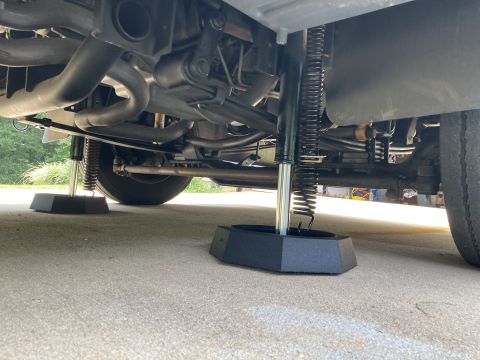 2015 Ford F-550 - The underside of an RV showing the extended leveling jacks with their bases on the concrete.