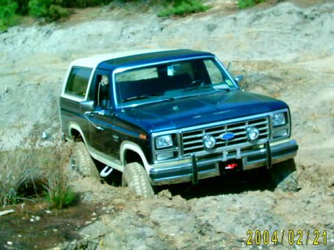 1985 Ford Bronco - This blue Ford Bronco, likely from the early 1980s, is navigating a challenging muddy terrain.