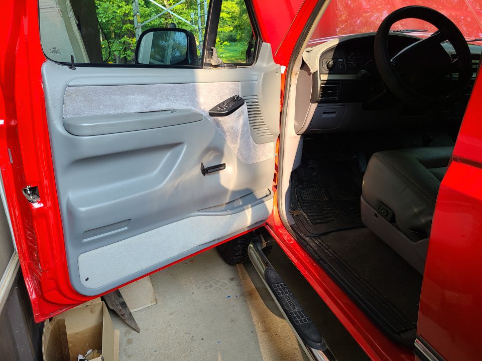 Red Ford F-Series truck interior, driver's side door open, showing gray door panel and dashboard