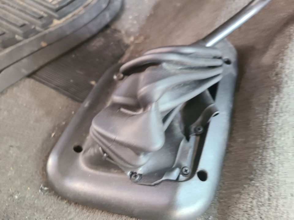 close-up of a black rubber gear shifter boot and its plastic base, with a floor mat visible to the left