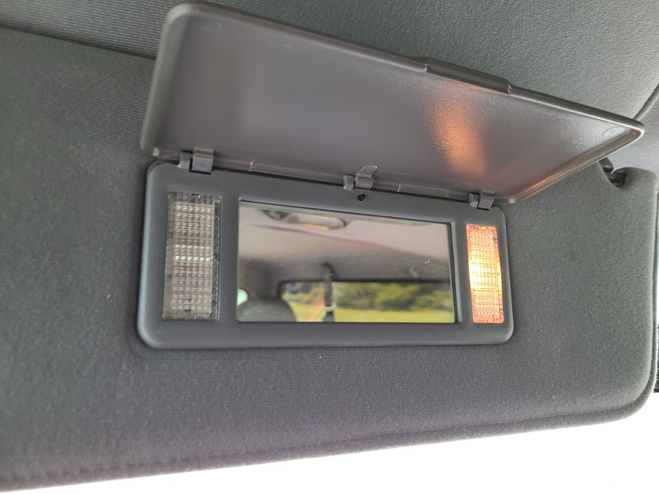 Open lighted vanity mirror on gray sun visor inside a vehicle, one light illuminated