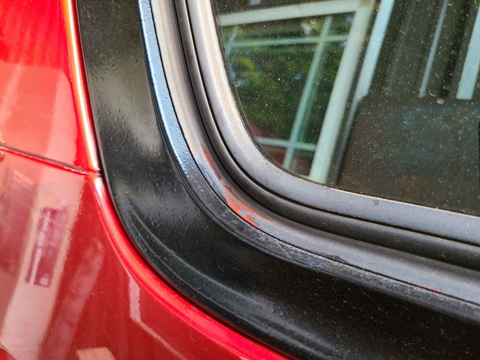 Close-up of black window seal corner on red vehicle with red paint visible on rubber trim