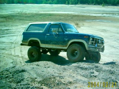 1985 Ford Bronco - A blue Ford Bronco with a lifted suspension navigates a dirt track in a clay pit.