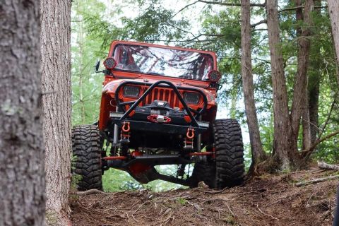1992 Jeep Wrangler - Orange 1992 Jeep Wrangler navigates a steep, wooded trail with aggressive off-road tires.