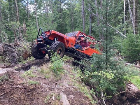 1992 Jeep Wrangler - This heavily modified off-road vehicle navigates a challenging incline on a dirt path surrounded by trees.