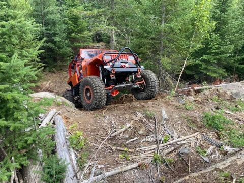 1992 Jeep Wrangler - An orange off-road Jeep tackles a challenging trail through a dense forest.