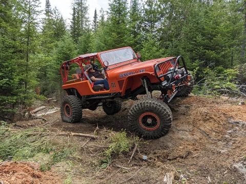 1992 Jeep Wrangler - This modified Jeep is navigating a steep, wooded trail with significant articulation.