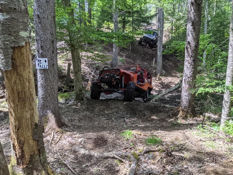 Orange off-road buggy navigating a wooded trail with another vehicle behind