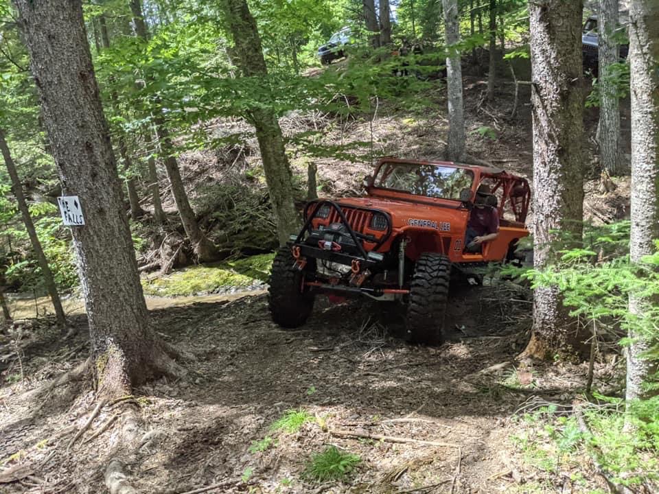 Orange 1992 Jeep Wrangler on a wooded trail, another vehicle visible in the background