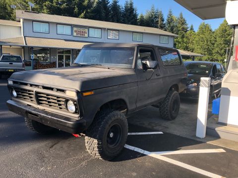 1978 Ford Bronco - A matte black Ford Bronco is parked at a gas station, with a general store in the background.