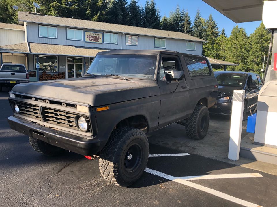 Black Ford Bronco parked at gas station, front end visible with grille and headlights