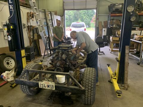 1979 Jeep CJ5 - Mechanics work on the engine of a 1979 Jeep CJ5 chassis in a garage, with a Texas license plate visible.