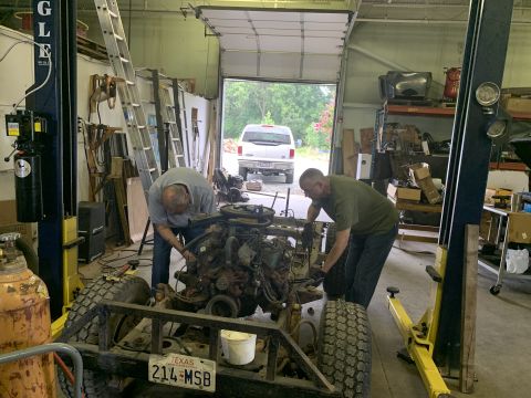 1979 Jeep CJ5 - Mechanics are working on a vehicle's engine and frame inside a garage.