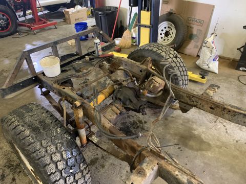 1979 Jeep CJ5 - The frame and suspension of a Jeep CJ5 are shown in a workshop, with tires and drivetrain parts visible.