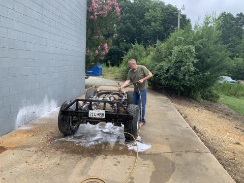 1979 Jeep CJ5 - A man pressure washes the frame of a Jeep CJ, which is missing its body panels and engine.