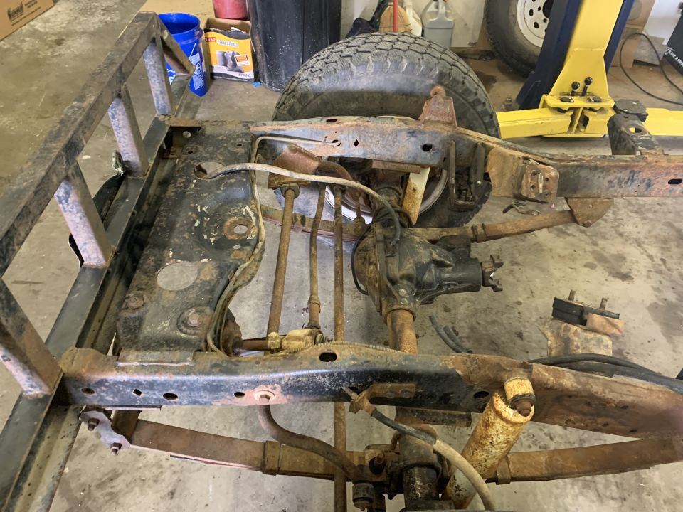 Jeep CJ frame with suspension components and a tire, showing rust and wear