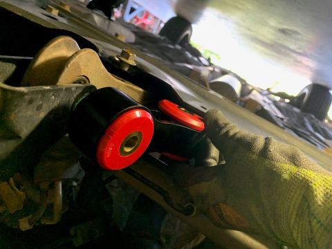 2008 Ford Focus - Close-up view of a gloved hand installing a red and black suspension bushing on the underside of a vehicle.