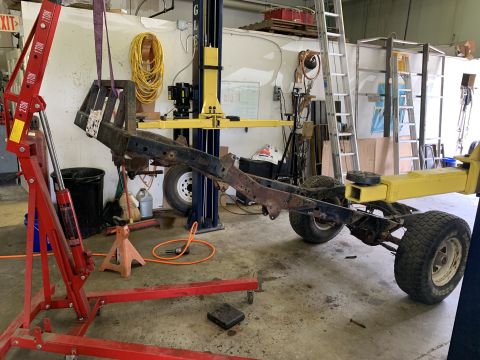 1979 Jeep CJ5 - The chassis of a vehicle is suspended by a red engine hoist, with a yellow vehicle lift visible behind it.