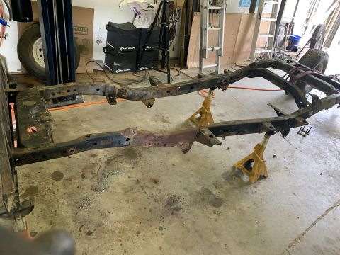 1979 Jeep CJ5 - The frame of a vehicle, likely undergoing restoration or repair, is supported by yellow jack stands in a garage setting.