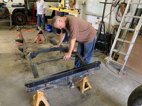 1979 Jeep CJ5 - A man inspects a vehicle frame supported by jack stands in a workshop setting.