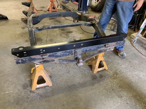 1979 Jeep CJ5 - The frame of a Jeep CJ is supported by jack stands in a workshop.