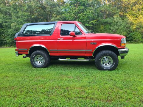 1995 Ford Bronco - This 1995 Ford Bronco is captured in a side profile, its iconic design and red exterior with a contrasting black top.