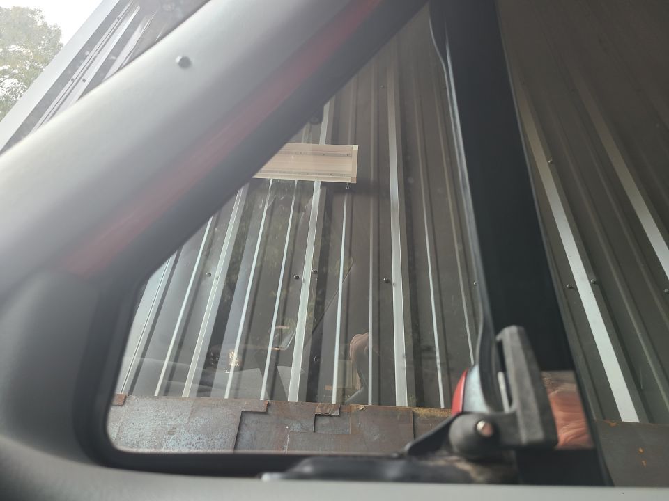 View through a vehicle's window showing a corrugated metal wall and a black interior trim piece