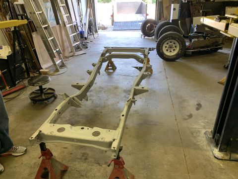 1979 Jeep CJ5 - A vehicle frame is supported by jack stands in a workshop, with various tools and parts visible around it.